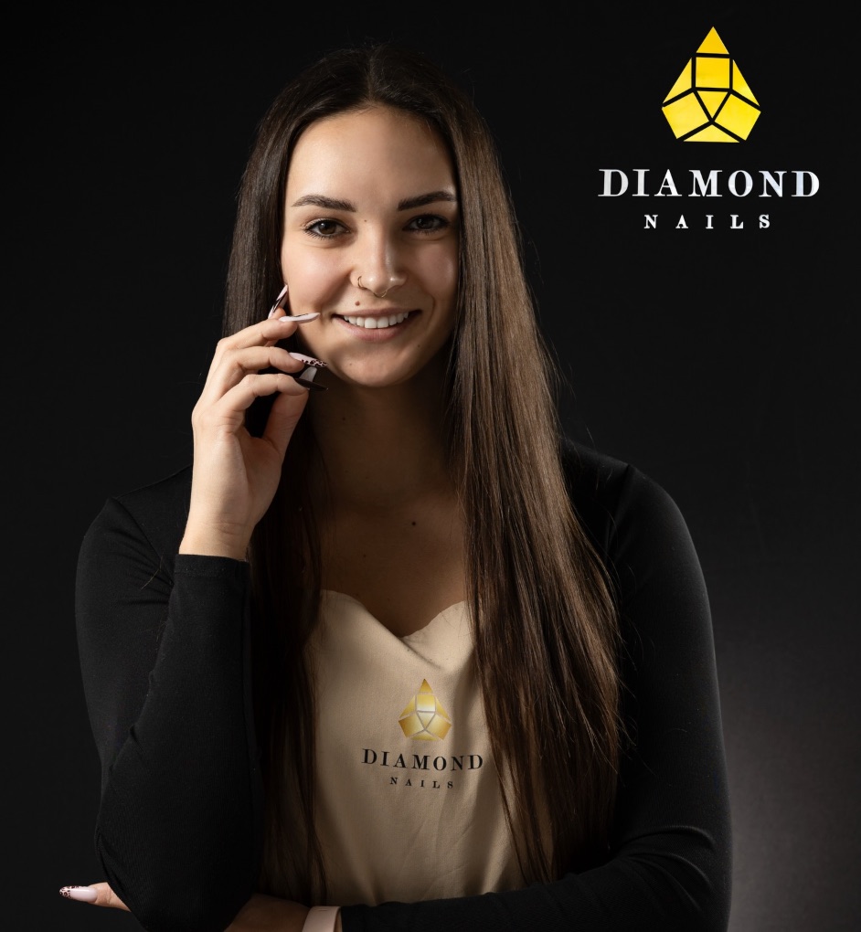 Paulina, stylistka Diamond Nails, uśmiechnięta, w beżowym fartuchu z logo salonu, na czarnym tle